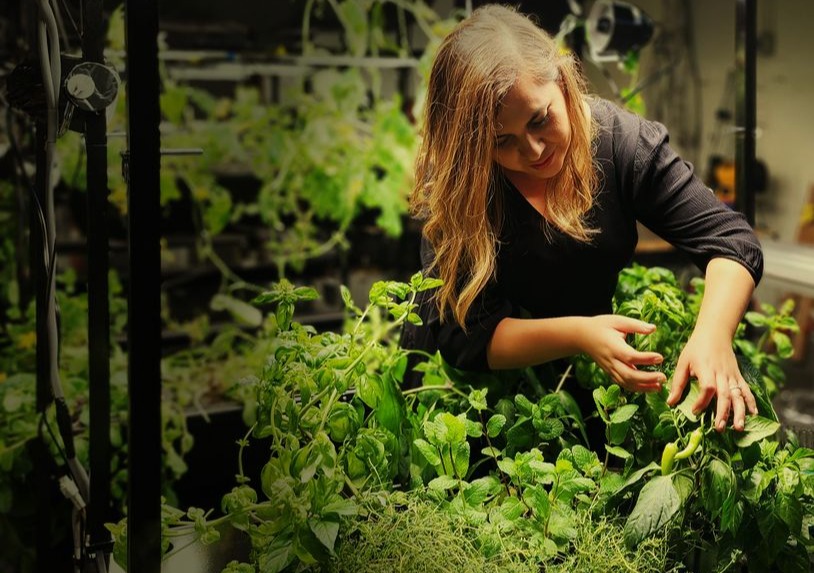 Woman in black shirt harvests from plants grown in Eden Grow Systems tower.